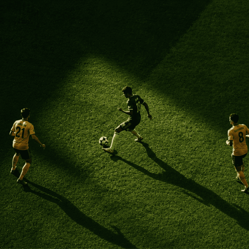 Aerial view of a soccer match: a player in dark jersey with the ball surrounded by two players in orange jerseys on a green pitch.